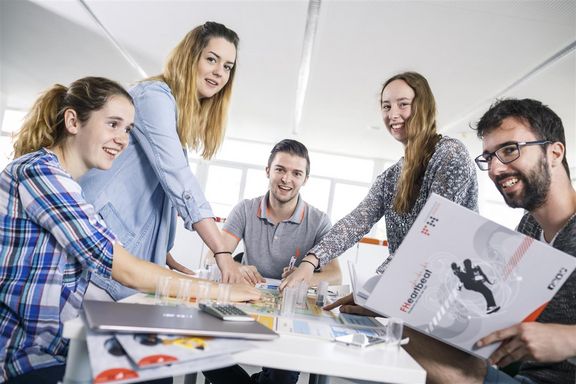 Das Imagefoto von Triple_E zeigt fünf Studierende die auf einen Gegenstand am Tisch zeigen.