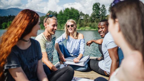 Foto von international Studierenden, die am Steg bei einem See sitzen