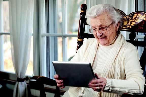 Das Imagebild von IARA zeigt eine lächelnde, alte Frau im Schaukelstuhl mit einem Tablet in der Hand