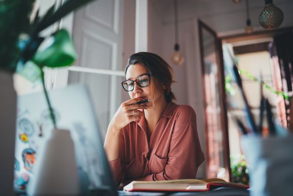 Digitalisierung & Business Development Junge Frau sitzt vor dem Laptop, Pflanze unscharf links im Bild