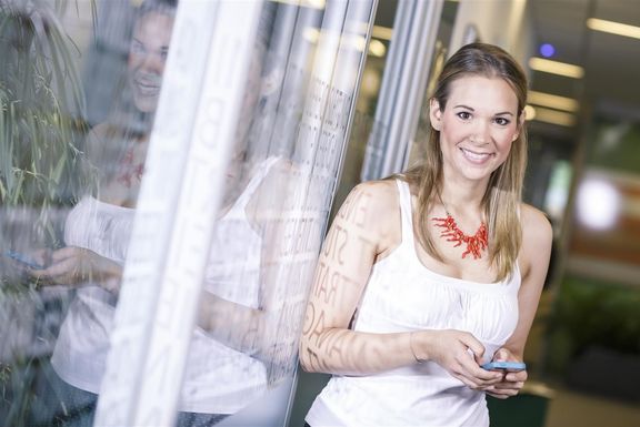 Wirtschaftsstudium FH - DTMO zeigt eine Studentin mit einem Smartphone in den Händen, die an einer Glastüre lehnt.
