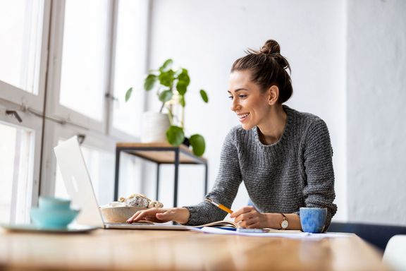 junge Frau am Schreibtisch mit Laptop und Teeschale, Pflanze im Hintergrund