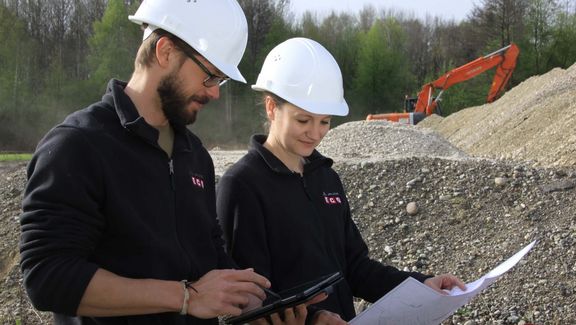 Naturschutzfachkraft: Junger Mann und junge Frau stehen in einem Schotterfeld und begutachten einen Plan